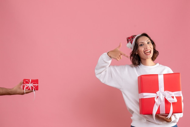 Front view of young woman holding present with man who's giving her other present on pink wall