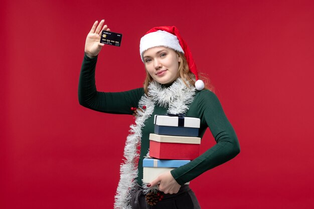 Front view young woman holding presents and bank card on red desk