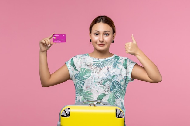 ピンクの壁の航海の色の休暇の女性の夏の旅行で休暇中に紫色の銀行カードを保持している正面図若い女性
