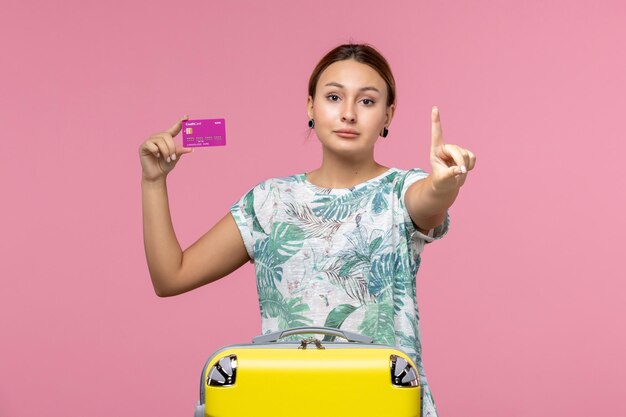 Front view young woman holding purple bank card on vacation on light pink wall color voyage vacation summer woman