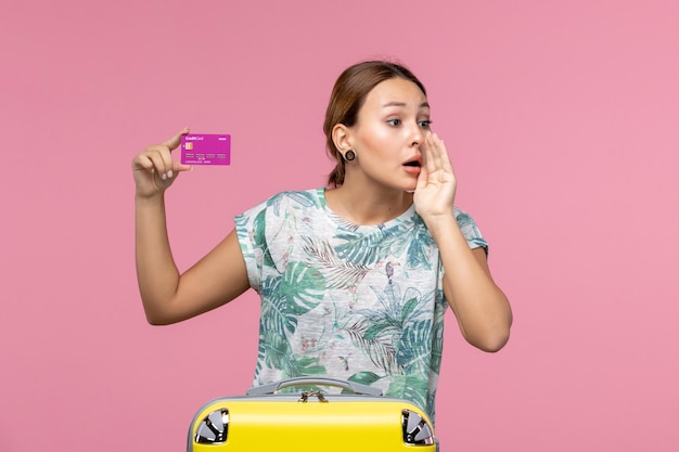 ピンクの壁の色の航海休暇夏の女性の休暇中に紫色の銀行カードを保持している正面図若い女性