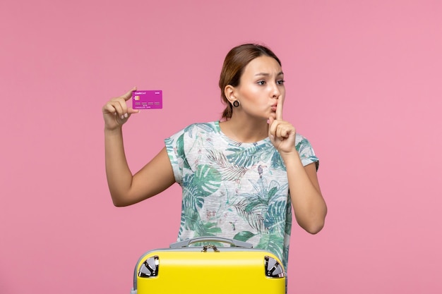 Front view young woman holding purple bank card on vacation on the pink wall color voyage vacation summer woman