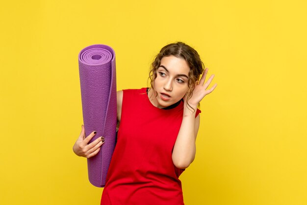 Front view of young woman holding purple carpet on a yellow wall