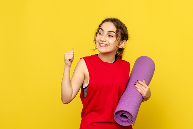 Front view of young woman holding purple carpet on a yellow wall