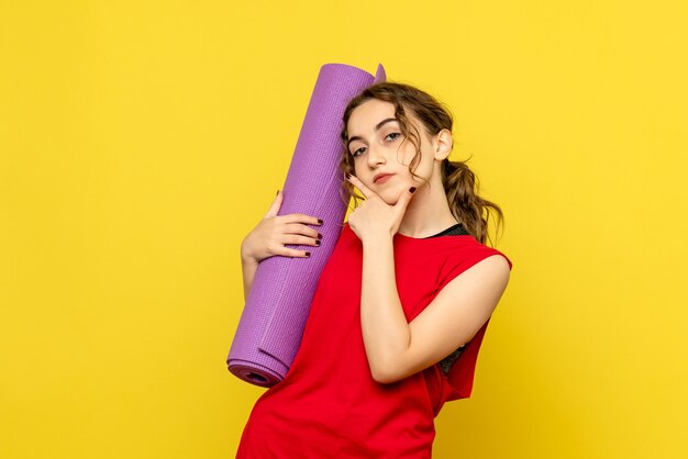 Front view of young woman holding purple carpet on the yellow wall