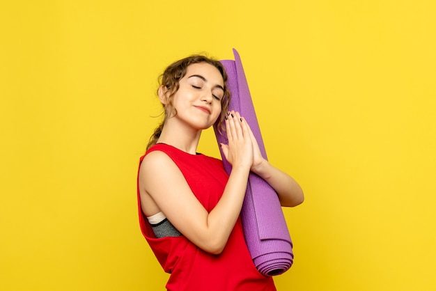 Front view of young woman holding purple carpet on yellow wall