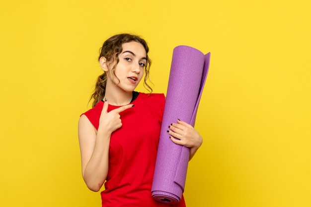 Free photo front view of young woman holding purple carpet on yellow wall