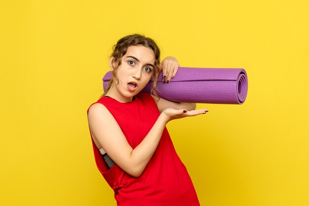 Front view of young woman holding purple carpet on yellow wall