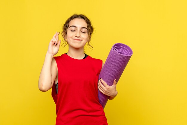 Front view of young woman holding purple carpet on yellow wall