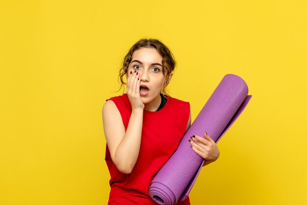 黄色の壁に紫色のカーペットを保持している若い女性の正面図