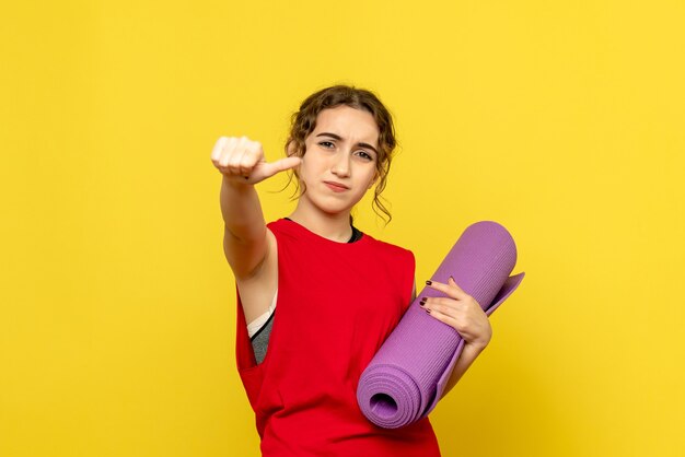 Front view of young woman holding purple carpet on yellow wall