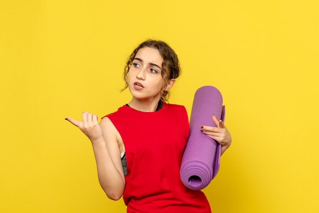 Front view of young woman holding purple carpet on yellow wall