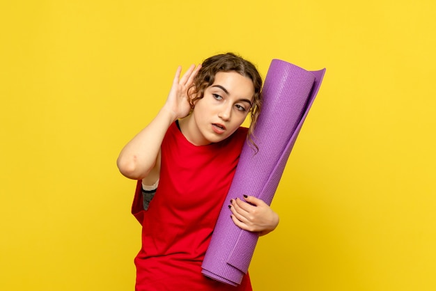 Free photo front view of young woman holding purple carpet on yellow wall