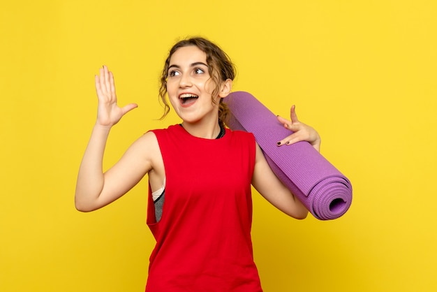 Front view of young woman holding purple carpet on yellow wall