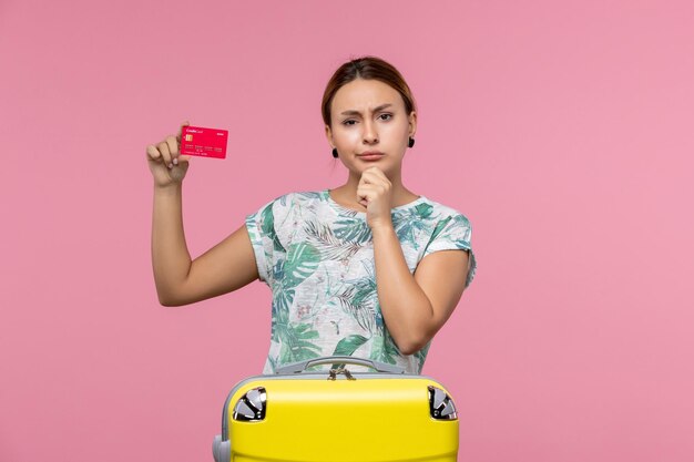 Front view young woman holding red bank card on vacation on light pink wall woman voyage plane flight vacation rest