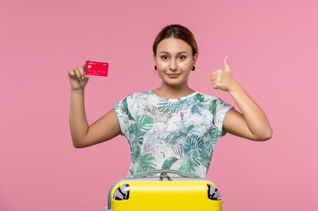Вид спереди молодая женщина, держащая красную банковскую карту в отпуске на розовой стене, рейс женщина, рейс, самолет, отдых, отдых