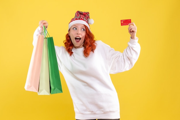 Front view of young woman holding shopping packages and bank card on the yellow wall