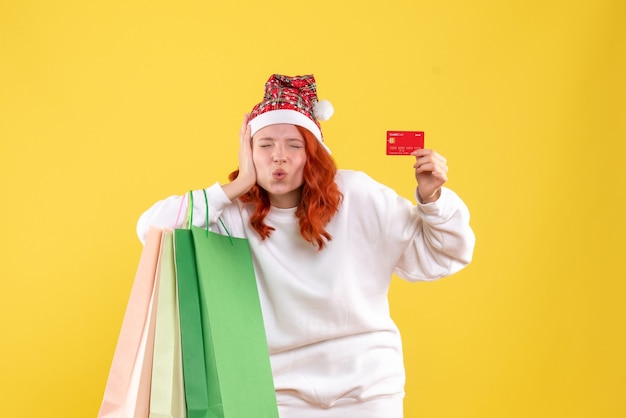 黄色の壁にショッピングパッケージと銀行カードを保持している若い女性の正面図