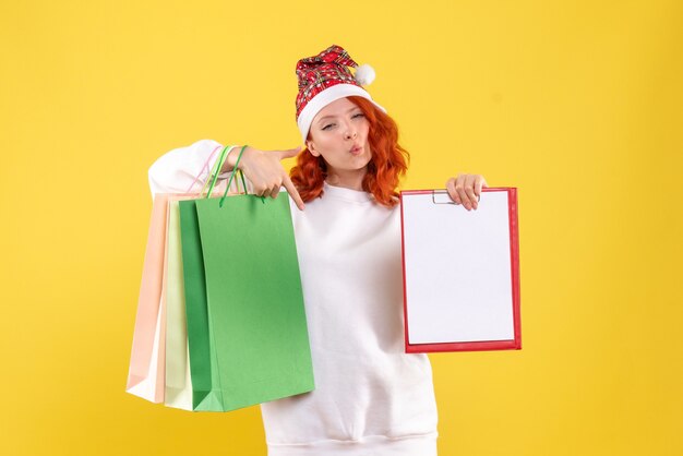 Front view of young woman holding shopping packages on a yellow wall