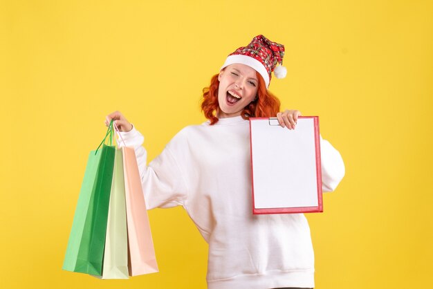 Front view of young woman holding shopping packages on yellow wall