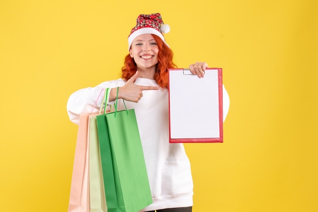 Front view of young woman holding shopping packages on yellow wall