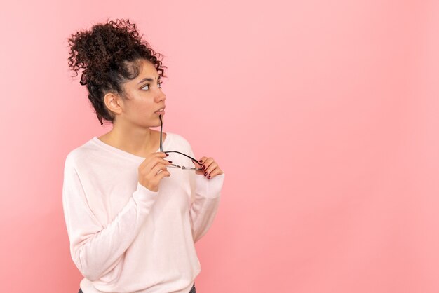 Front view of young woman holding sunglasses on pink wall