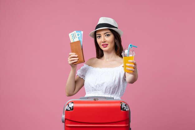 Вид спереди молодая женщина, держащая билеты и коктейль в летние каникулы на розовом полу, вояж, отпуск, летняя поездка, жара, цвет