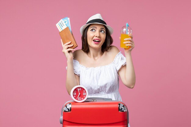 ピンクの壁の旅の女性の休暇の航海夏の暑さで休暇中にチケットとカクテルを保持している正面図若い女性