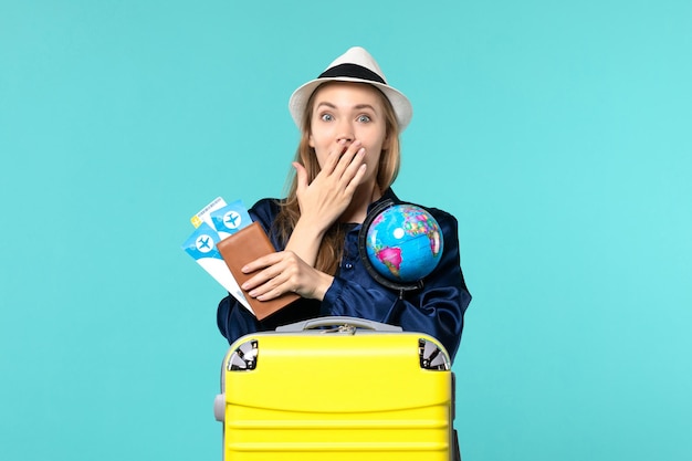 Вид спереди молодая женщина, держащая билеты и глобус на голубом фоне, самолет, рейс, море, отпуск, путешествие