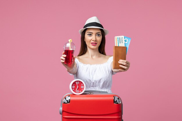 Вид спереди молодая женщина, держащая билеты и сок на отдыхе на розовой стене, путешествие, летняя женщина