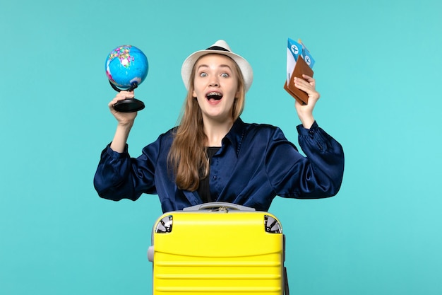 Vista frontale della giovane donna che tiene i biglietti e piccolo globo sul mare di viaggio di viaggio di viaggio di vacanza di sfondo blu chiaro