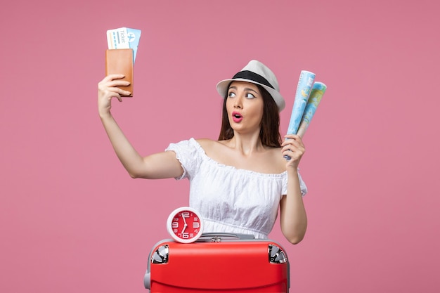 Front view young woman holding tickets and map on vacation on a pink wall vacation trip summer heat voyage woman