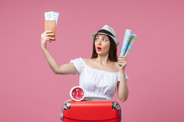 Вид спереди молодая женщина, держащая билеты и карту в отпуске на розовой стене, отпуск, летняя жара, путешествие, женщина