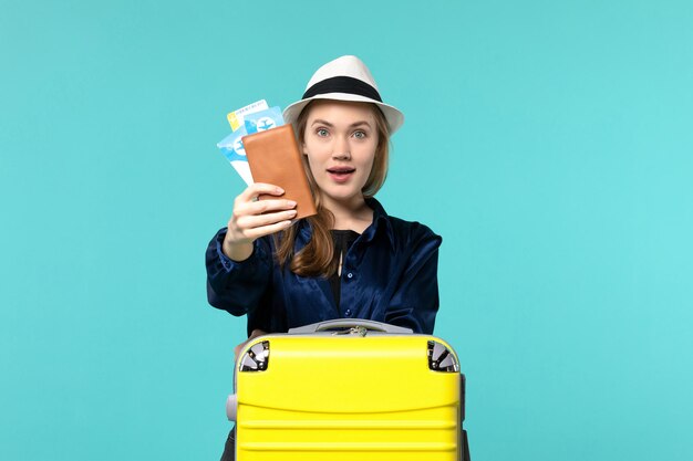 Вид спереди молодая женщина, держащая билеты и готовящаяся к поездке на синем фоне, путешествие на море, отпуск, путешествие на самолете