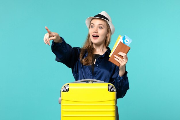 Вид спереди молодая женщина, держащая билеты и готовящаяся к поездке на синем фоне, путешествие на море, отпуск, путешествие, путешествие