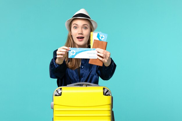 Вид спереди молодая женщина, держащая билеты и готовящаяся к поездке на синем фоне, путешествие, путешествие, самолет, море, отдых, путешествие