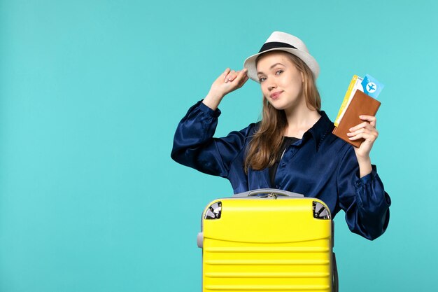 Вид спереди молодая женщина, держащая билеты и готовящаяся к отпуску на синем фоне, путешествие на море, отпуск, самолет, путешествие, путешествие