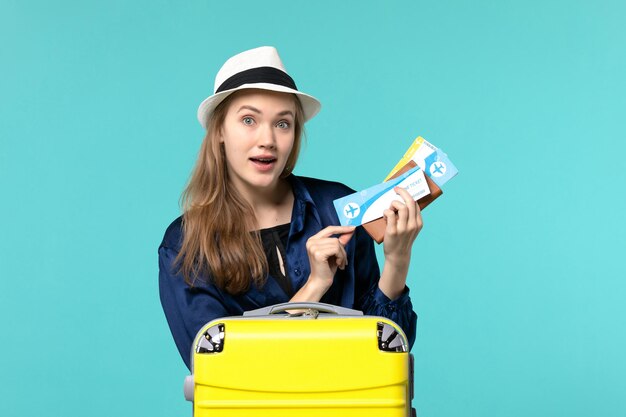 Вид спереди молодая женщина, держащая билеты и готовящаяся к отпуску на синем фоне, морское путешествие, путешествие, самолет, отдых