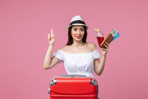 Вид спереди молодая женщина, держащая билеты в отпуске на светло-розовой стене, путешествие, женщина, отдых, путешествие, лето