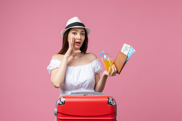 Front view young woman holding tickets for vacation and posing on light-pink wall summer trip emotion plane voyage