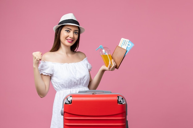 Front view young woman holding tickets for vacation and posing on pink desk summer trip emotion plane voyage