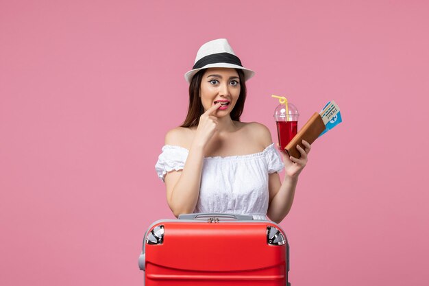 淡いピンクの壁の女性の夏の旅行の残りの航海で休暇中にジュースとチケットを保持している正面図若い女性