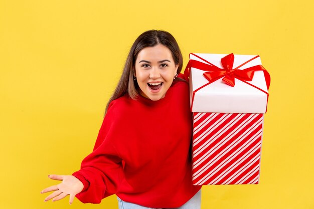 黄色の壁のボックスにクリスマスプレゼントを保持している若い女性の正面図