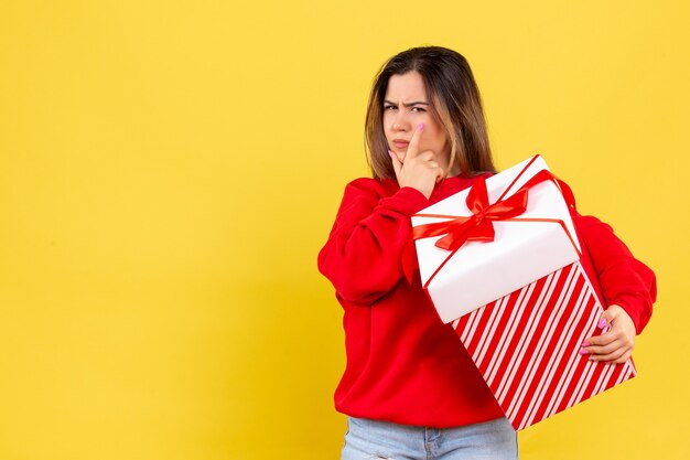 Front view young woman holding xmas gift thinking on yellow background