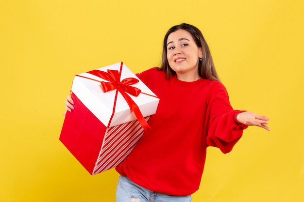 Front view young woman holding xmas gift on a yellow background