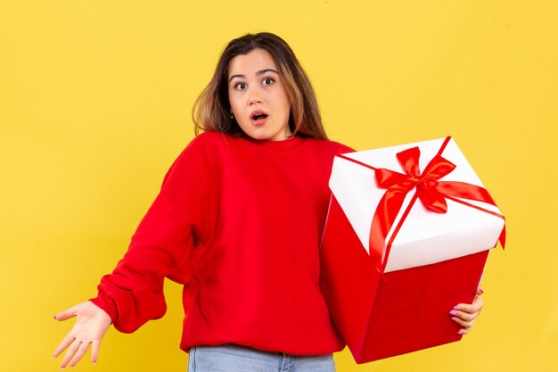 Front view young woman holding xmas gift on the yellow background