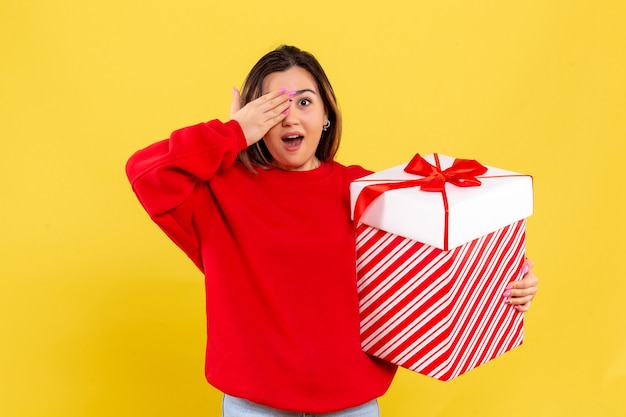 Free photo front view young woman holding xmas gift on yellow background