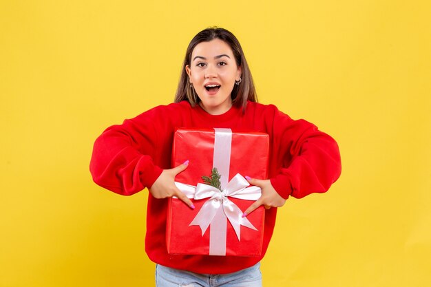 Front view young woman holding xmas gift on yellow background