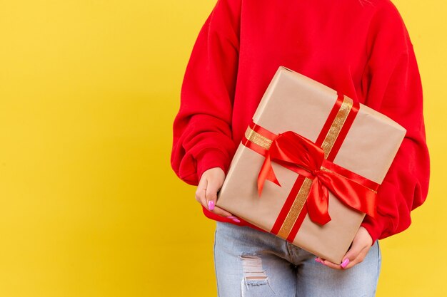 Front view young woman holding xmas gift on yellow background