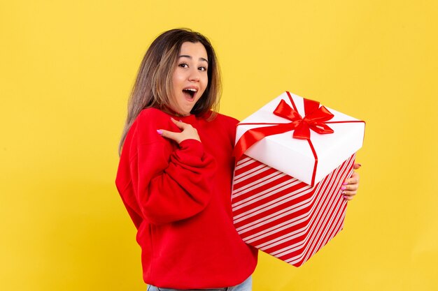 黄色の背景にクリスマスプレゼントを保持している正面図若い女性